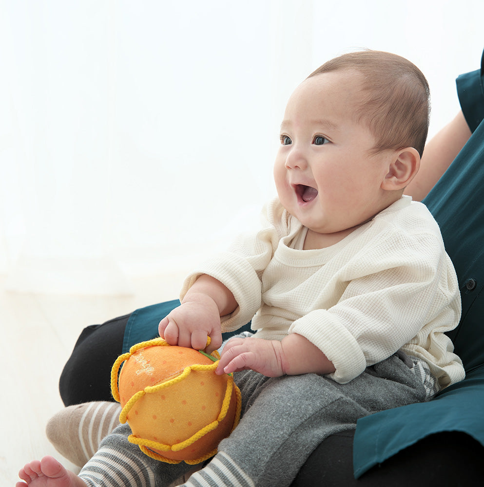 両手でわっかボールみかんを持つ赤ちゃん