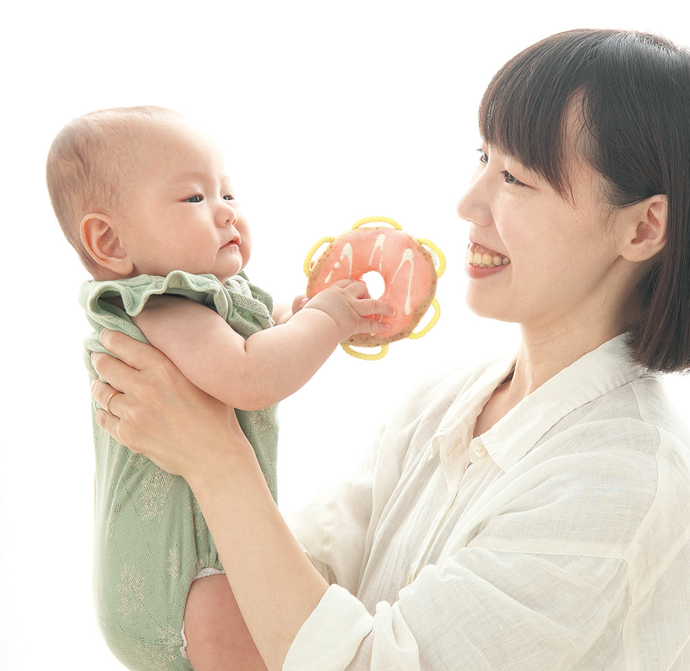 わっかラトルドーナツを持つ赤ちゃんを抱っこするお母さん